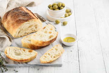 Ciabatta. Italian bread with olive oil, herbs and olives on a marble table. Space for text - obrazy, fototapety, plakaty