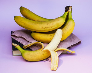 A branch of bananas on a cloth napkin, next to an open banana on a pink background. the style of minimalism.