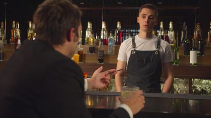 Man sits at the bar, holds credit card and quarrels with bartender 