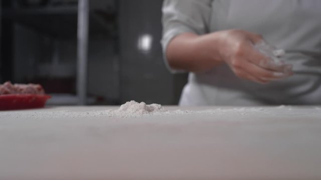 Close-up: women's hands scatter baking flour on the table. A female cook is preparing for cooking. A scattering of white wheat flour on the table. Slow motion, 4K, Red Epic
