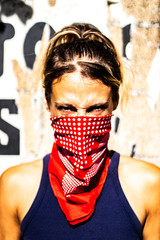 Extreme close up portrait on the face of an angry young activist and feminist woman with blond hair and her red bandana on her face, screaming and looking at the camera, liberty and girl power 