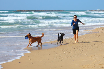 Mature Woman  playing with her dogs on the beach.