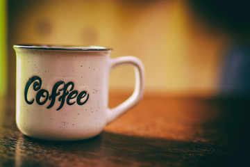 Enamel white metal mug with  inscription  coffee on  wooden table on blurred background. White cup of coffee on a dark background. Place for text or advertising