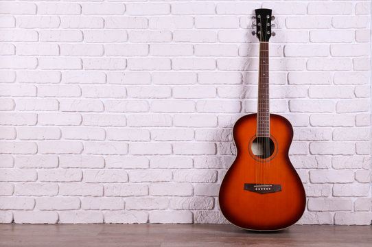 Folk style parlor acoustic guitar over white brick wall background with a lot of copy space for text. Studio shot of travel size musical instrument. Close up. © Evrymmnt