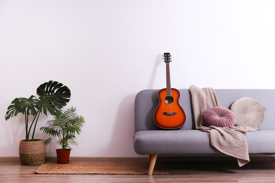 Minimalistic interior design concept. Acoustic guitar on grey textile sofa in spacious room of loft style apartment with wood textured laminated flooring. Background, copy space, close up. - Powered by Adobe
