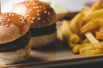 Small beef burgers with cereals bread, cheese,  served on a little cutting board with sauces, fries