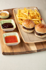 Small beef burgers with cereals bread, cheese,  served on a little cutting board with sauces, fries