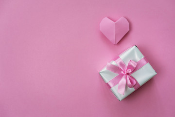 Minimalistic Valentine's Day background with a gift box wrapped with ribbon and origami heart.