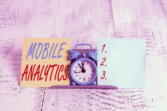 Conceptual hand writing showing Mobile Analytics. Concept meaning studies the behavior of mobile website visitors and users Mini blue clock standing above buffer wire between two paper