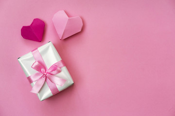 Valentine's Day romantic flat lay photo with a gift box and ribbon, origami hearts, copy space on right side.