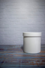 White plastic jar on a wooden table on a background of a white brick wall. Copy space. place for text