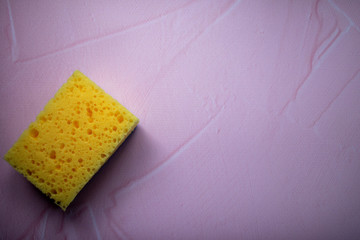 Yellow foam sponge for washing dishes and cleaning. Soft washcloths on a pink background top view.