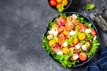 Fresh rainbow salad with feta cheese and lemon dressing on dark background. Top view, space for text.