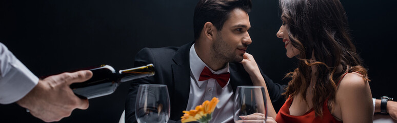 Selective focus of smiling couple at table beside waiter pouring wine in glasses isolated on black