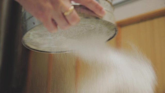 Baker sifting wheaten flour and preparing dough for making cake