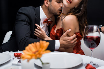 Selective focus of elegant man kissing in neck woman at served table isolated on black