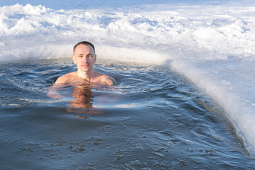 Winter swimming in cold water. The guy bathes in the ice hole under the bright winter sun