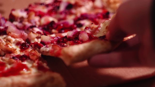 Close-up of hands taking a pizza slice with chicken, pineapple and cowberry