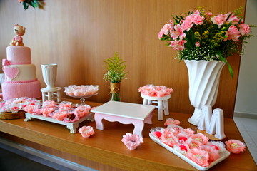 Bench decorated with vase of flowers, and other artifacts including plates with pink candies. Beautiful decoration for a party. 