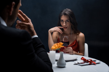 Selective focus of seductive woman with finger by lips looking at man during romantic dinner isolated on black