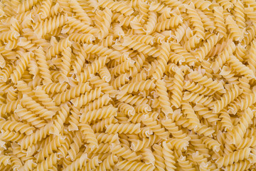 Raw dried extruded fusilli pasta texture. Staple food of Italian cuisine. Culinary background from short uncooked helical pastas for cooking side dishes. Use for recipe, packaging design, gastronomy.
