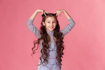 Girl 7 years old beautiful smiling makes a heart sign with her hands. Friendly brunette schoolgirl with long hair. The concept of St. Valentine on February 14. Friendliness love kindness. Denim