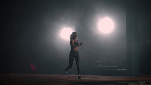 A sporty woman runs up in a stadium and performs a long jump in slow motion in a stadium on a dark background