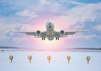 White passenger aircraft take off from winter airport runway against the backdrop of a scenic evening sky with sun rays