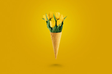 Yellow beautiful tulips in an ice cream waffle cone on a yellow background. Conceptual idea of a...