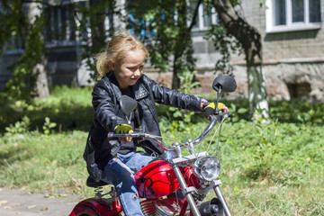 Fototapeta na wymiar little girl biker child in a leather motorcycle jacket rides a children's red cool electric bike chopper motorcycle and poses in clothing style motorcyclists