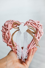 Girl holds a pink heart with decoration. Rattan knitted heart for decoration.