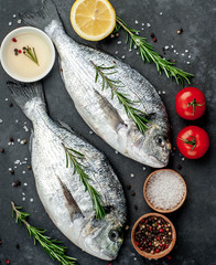 Fresh dorado fish with spices and ingredients tomato, razmorin, sunflower oil, lemon for cooking on a stone background