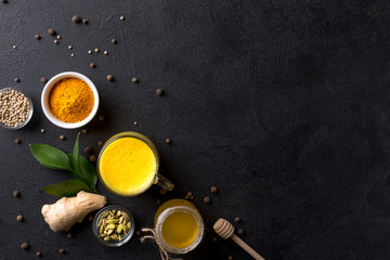 Cup with golden latte, honey, turmeric, cardamom and ginger on black background.