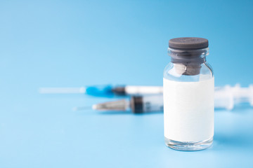Medical glass bottle with copy space, on a blue background with syringes. Selective focus. Medical...