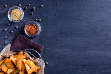 Baked potato wedges in a pan and spices on a black wooden background. Background menu food.