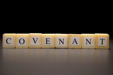 The word COVENANT written on wooden cubes isolated on a black background...