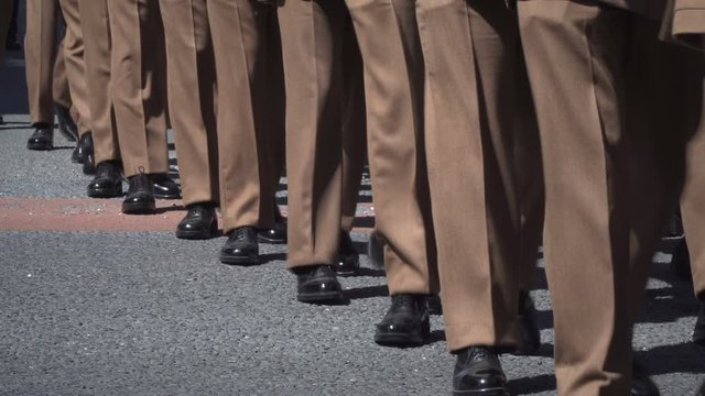 Army Soldiers parade through the streets in homecoming parade. They march in formation in brown uniform. Marching