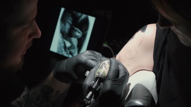 Footage of man doing black tattoo of snake in studio