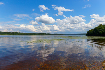 Picturesque clouds are reflected in the water of the Volga. The bottom of the river is visible through the clear water. The panorama is made in warm summer weather. Ivanovo region, Russia.