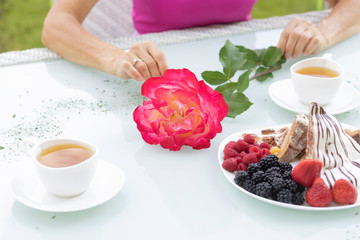 female hands hold a flower next to two cups of herbal tea and a yogurt cake with berries on a white table. The concept of date, holiday, romantic, Valentine's day. Happy woman in love