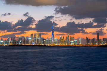 Fototapeta premium Piękny zachód słońca nad kultowymi budynkami Dubaju. Niesamowite szare chmury i pomarańczowe niebo. Nowoczesna i luksusowa panorama miasta z Dubai Creek.