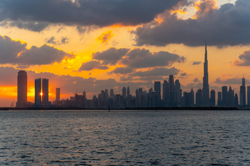 Colorful sunset over the iconic buildings of Dubai. Amazing gray clouds and orange color sky. The modern and luxury cityscape panorama view from Dubai Creek.