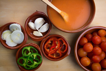  Fresh ingredients for cold tomato soup, tomatoes, peppers, onion, garlic, olive oil. On a wooden table and clay utensils