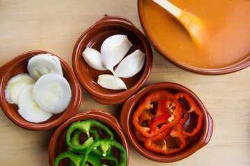  Fresh ingredients for cold tomato soup, tomatoes, peppers, onion, garlic, olive oil. On a wooden table and clay utensils