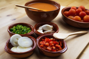  Fresh ingredients for cold tomato soup, tomatoes, peppers, onion, garlic, olive oil. On a wooden table and clay utensils