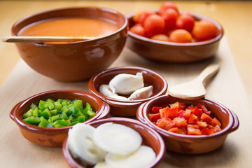  Fresh ingredients for cold tomato soup, tomatoes, peppers, onion, garlic, olive oil. On a wooden table and clay utensils