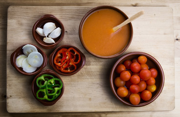  Fresh ingredients for cold tomato soup, tomatoes, peppers, onion, garlic, olive oil. On a wooden table and clay utensils