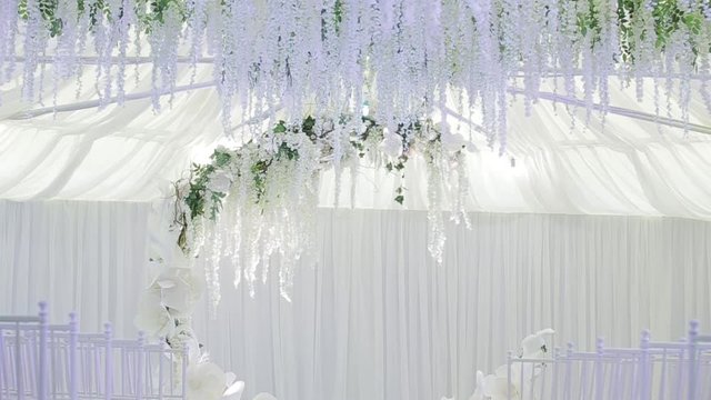 Large spacious white wedding room with a large wedding cute wreath, under which the bride and groom become. White chairs for guests. Happy day for the newlyweds. Wedding party after the ceremony.