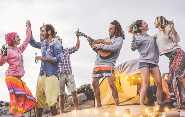 Group friends doing party playing guitar and camping outdoor - Happy young people having fun drinking beer and laughing in camp village - Youth culture lifestyle and vacation travel concept