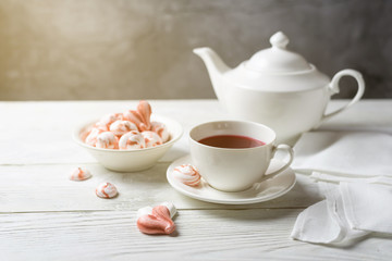 Obraz na płótnie Canvas Beautiful romantic breakfast with red tea Hibiscus and meringue cookies in the shape of hearts and candy. White tea-set stand on a wooden table with a sunlit. Still life with copy space.